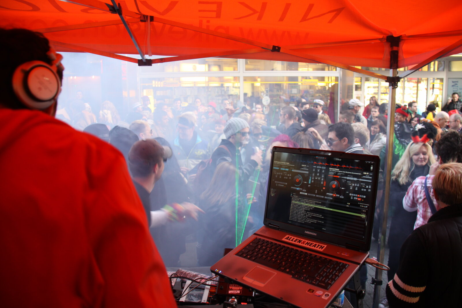 DJ booth de rue sous tente rouge, foule en plein jour, fumée et lasers